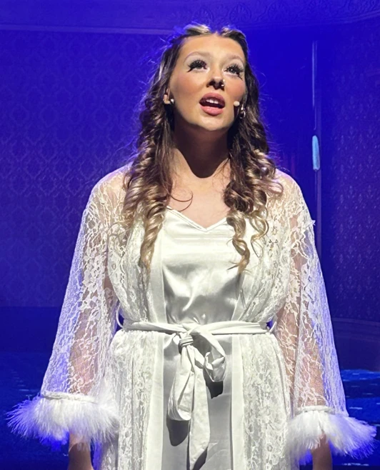 Actor singing solo on stage, dressed in elegant white robes with delicate lace trim. Actor singing solo on stage, dressed in elegant white robes with delicate lace trim.